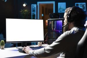 Man using gaming station mockup monitor, excited to finally relax by playing videogame on PC at computer desk late at night. Gamer starting game on isolated screen computer, battling foes photo