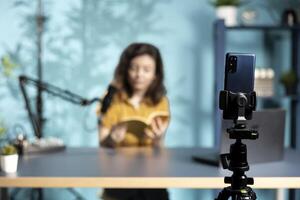 Focus on smartphone used by content creator to film review of book, browsing through pages. Close up of phone used by online star to record impressions of new novel release photo