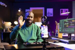 Skilled audio engineer teaching online mixing tunes lessons by using a smartphone on tripod to record himself in home studio. Producer hosting a master class with soundboard console gear. photo