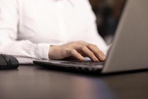 A closeup of a woman typing on her laptop, her fingers swiftly navigating the keyboard as she inputs financial data. The selective focus draws attention to her hands in a modern office. photo