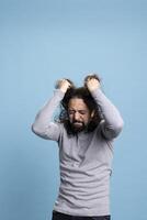 Distraught upset guy acting crazy and pulling his hair in front of camera, being overwhelmed and furious with intense emotions. Annoyed man with an aggressive reaction and rage in studio. photo