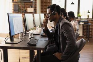 Male customer support agent looking at computer screen showing financial data and statistics, tracking performance ratings. African american man, focused in his work, reviewing data on desktop monitor. photo