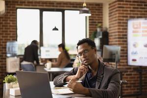 African American employee with pen in hand, providing insights to a client on a call, discussing business growth. Black man in wheelchair using a landline phone while reviewing company research data. photo