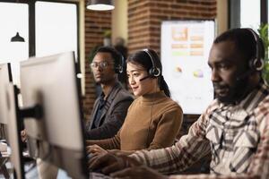 Selective focus of female employee working together with african american colleagues, providing remote client support. Asian woman analyzing customer feedback on a desktop computer. photo
