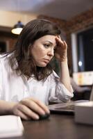 Stressed woman working late in modern office, managing heavy responsibilities under pressure. Closeup of female employee showing signs of fatigue and burnout during night shift, trying to concentrate. photo