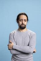 Depressed anxious adult dealing with low self esteem against blue background, whining and being in an emotional crisis. Melancholic person with distress and desolation, disappointed guy. photo