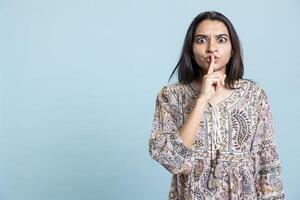 Private person doing mute silence hand gesture in front of camera, demanding secrecy and being irritated by noise. Indian person complaining, placing finger on lips and doing quiet warning sign. photo