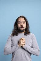 Astonished man having an unexpected unbelievable reaction on camera, feeling amazed with open mouth against blue background. Stunned ecstatic person excited and surprised about something. photo