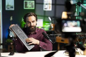 Content creator filming keyboard review in personal studio, pressing different buttons to show typing capabilities. Technology guru showcasing computer peripheral to audience on niche online channel photo