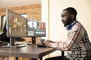 Black male editor with headphones, enhancing quality of digital footage on computer screens. African american production specialist using multi monitor setup to refine movie frames. photo