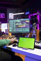 Producer songwriter mixing and mastering tracks with stereo gear, greenscreen layout on a tablet. Sound engineer improving audio quality, acoustical engineering in post production. photo