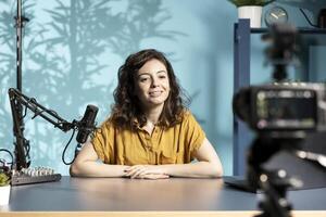 Cheerful content creator using high tech quality mic in studio to do ASMR , discussing with viewers. Smiling woman using professional microphone to record podcast in studio photo