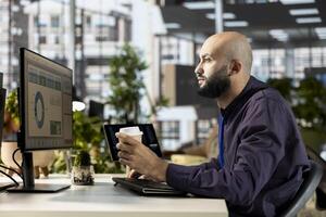 Middle eastern office employee working with monthly revenue balance to create financial plans using online tools, reviewing data analytics. Young businessman manages objectives for success. photo