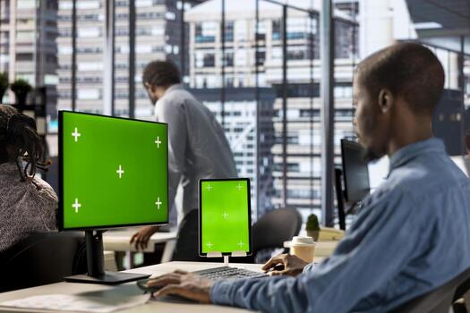 Businessman seated at workstation with green screen on devices, working on solving administrative tasks for enterprise growth. Developing performance metrics to support project goals. photo