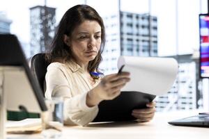 Female leader with executive power signing work contracts and approving employees requests, doing daily paperwork tasks for productivity. Giving authorization for leave request or license agreement. photo