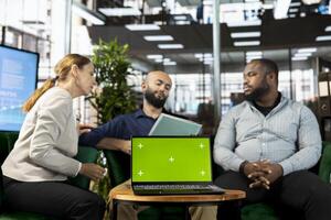 Green screen laptop in front of businesspeople talking in startup company, looking at financial business documents. Chroma key notebook used by diverse team of office clerks photo