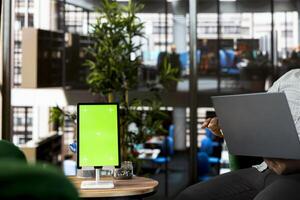 Green screen tablet and laptop used by staff member preparing for business meeting. Mockup device next to office clerk using notebook in startup to do research analysis, reading documents online photo