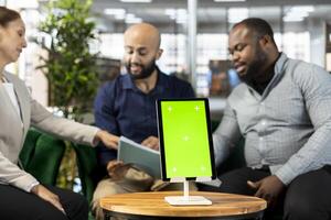 Isolated screen tablet next to workers looking over research documentation needed for finding business insights and finishing project task. Employees analyze data on mockup device and paperwork files photo