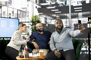 Man and colleagues talking selfie picture after successful briefing meeting to share ideas for profit growth. Employees in office talking photos with smartphone after working on startup evolution vision