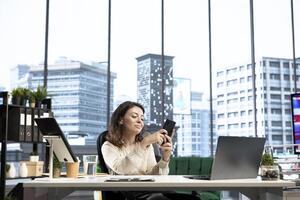 Female CEO taking a break from work and answering text messages on her smartphone, discussing with partners or friends in her high end business office. Social media updates online. photo