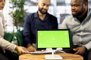 Green screen device next to teamworking colleagues in office coordinating company administrative operation. Close up of mockup tablet used by multiracial coworkers reviewing business data metrics photo