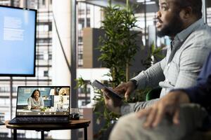 African american manager holding online conference meeting with remotely working workers. Teleworking executive in stylish office discussing with employees during call photo