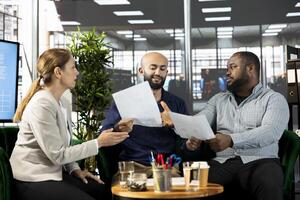 Multiethnic businesspeople in startup company looking at financial business documents. Workers in office checking accounting figures, finishing tedious paperwork, talking about data, doing comparison photo