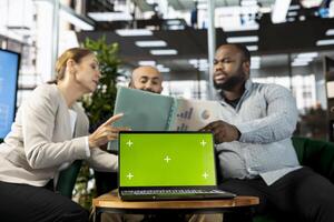 Green screen laptop in front of employees checking progress done on customer commissioned project. Chroma key notebook next to office clerks reading data statistics on paperwork after business audit photo
