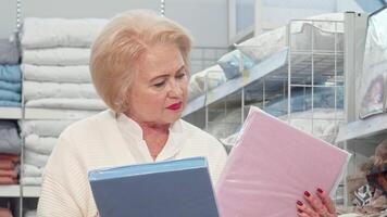 Charming senior lady selecting colorful bedding at a cozy furniture store video