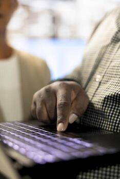 African american man next to colleagues in office coordinating company administrative operation, writing documents on notebook. Close up of employee typing on laptop keyboard, inputting data metrics photo