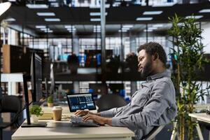 Male executive analyst finalizes a financial report and reviews data, developing a forecast for organizational progress. Black man engaged in task management and strategy planning. photo