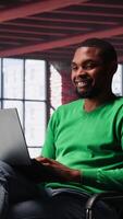 Vertical African american guy in loft opening laptop in the morning to work, browsing internet and researching information online. Teleworker starting job shift, using search engine on pc. Camera A. video