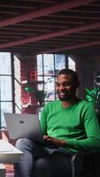Vertical African american guy in loft opening laptop in the morning to work, browsing internet and researching information online. Teleworker starting job shift, using search engine on pc. Camera B. video