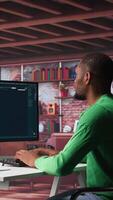 Vertical African American worker using program with photos in a modern loft. Young man creating visual content with deep learning models and prompts on monitor with AI interface. Camera B. video