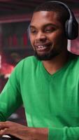 Vertical Smiling person in modern loft wearing headphones and listening to music during relaxation time, feeling pleased. Happy guy having fun at home with exciting songs through audio headset. Camera A. video