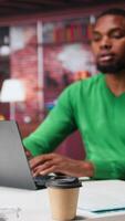 Vertical African american employee seated at home office using his pc, checking emails and answering messages in inbox. Remote worker managing electronic correspondence, tech savvy. Camera A. video