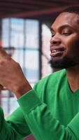 Vertical Man at home using smartphone to compose social media posts, producing content as a freelancer. African american guy monitoring profile engagement using mobile phone. Camera A. video