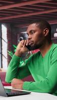 Vertical Freelancer in home office having important phone call with business partner using his mobile phone. African american guy sitting at desk discussing company matters during call. Camera A. video