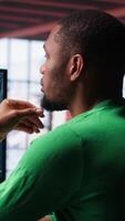Vertical Black guy uses deep learning tools to generate footage from text prompts in a productive home environment. Freelancer uses computer to display montage. Camera A. video