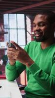 Vertical Man taking break from work to check his social media apps on mobile phone, having fun relaxing at home. Young guy in loft pausing tasks to use social network application on phone. Camera B. video