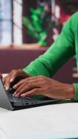 Vertical African american teleworker typing ideas to create a vision board on laptop, writing down his dreams and goals aligned with the company objectives. Remote worker connected from his home. Camera B. video