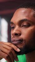 Vertical African american guy thinking about new ideas to increase clients numbers, multitasking to find a solution for financial growth. Young remote worker uses his creativity. Camera A. video