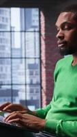Vertical African american remote worker solving daily job assignments, finishing his tasks online from the comfort of his modern loft. Young adult teleworker connected on web, multitasking. Camera B. video