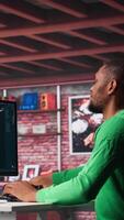 Vertical African American worker using program with photos in a modern loft. Young man creating visual content with deep learning models and prompts on monitor with AI interface. Camera A. video
