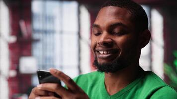 Man taking break from work to check his social media apps on mobile phone, having fun relaxing at home. Young guy in loft pausing tasks to use social network application on phone. Camera A. video