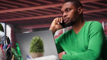 Freelancer in home office having important phone call with business partner using his mobile phone. African american guy sitting at desk discussing company matters during call. Camera B. video
