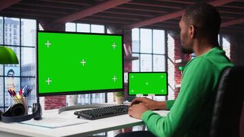 Black male worker in his loft using copy space PC to analyze sales reports and plan business growth, remote job. Young man working from home doing project research, typing on computer. Camera B. video