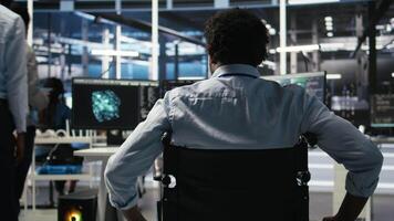 Server hub programmer with paraplegia in wheelchair uses AI machine learning node tree software. Man with disability in inclusive data center analyzes equipment issues using AI visualization, camera A video