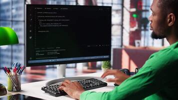 Male programmer types code on computer and running script, programming language. African american IT expert in modern loft fixing errors within the software, implementing new features. Camera A. video