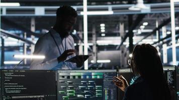 Server hub manager talking with programmer using node tree software to optimize system health. Data center supervisor overseeing IT expert analyzing equipment issues using AI visualization, camera B video